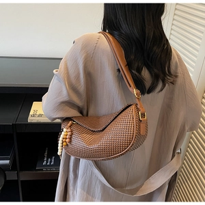 Brown woven half-moon shoulder bag with beaded fringe tassel worn by a model