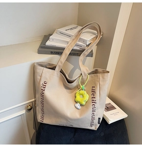 Close-up of beige canvas tote with black lettering and a yellow floral bag charm