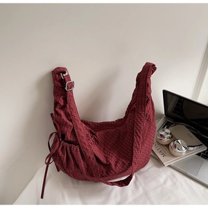 Detail of red checkered canvas shoulder bag showing adjustable strap and drawstring texture
