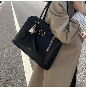 Close-up of black suede tote bag featuring a gold buckle strap and baseball glove charm