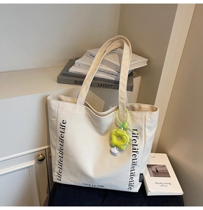 Close-up of cream canvas tote bag with black lettering and yellow sunflower charm detail