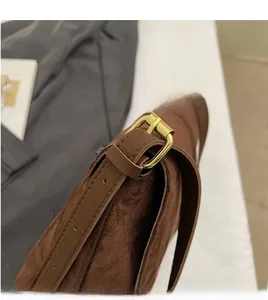Detail of brown matte suede shoulder bag featuring an adjustable gold metal buckle strap