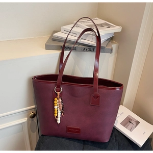 Détail du sac cabas bordeaux texturé avec charme à franges perle et étiquette logo