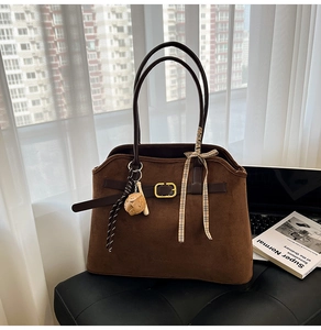 Detail of a brown suede tote bag with slender dark brown handles and a gold buckle accent