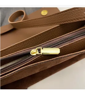 Detail of smooth gold metal zipper on a dark brown suede and textured leather crossbody bag
