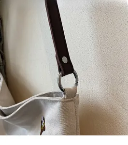 Detail of silver metal rings connecting brown leather straps to the beige canvas tote bag