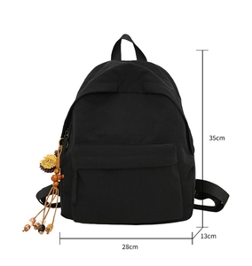 Detailed view of black nylon backpack dimensions with ethnic tassel charm on white background