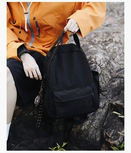 Detail of minimalist black backpack with front pocket and woven rope charm on side