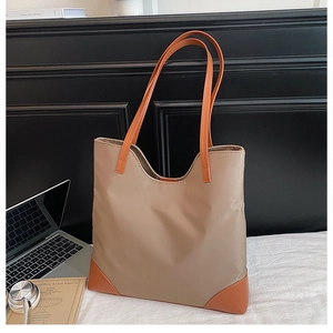 Detail of khaki nylon tote bag with orange handles and laptop in a lifestyle setting
