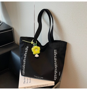 Detail of black canvas tote bag with LifeLifeLife print and a yellow sunflower charm