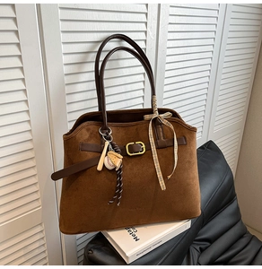 Detail of dark brown suede tote bag with leather handles and baseball charm accessory