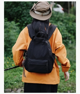 Outdoor view of a black minimalist waterproof backpack on a person wearing an orange jacket