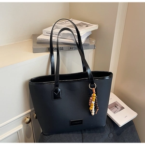 Détail du cabas noir avec breloque en perles et texture à grain croisé sur un bureau