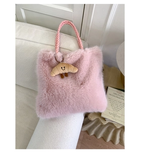 Pink plush handbag with woven handle and smiling croissant charm on white sofa