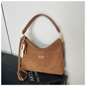 Detail einer braunen Wildleder-Hobo-Tasche mit Lederriemen und dekorativem Perlenanhänger