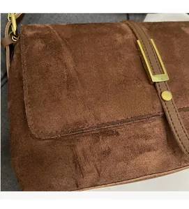 Detail of dark brown suede crossbody bag with matte texture and gold buckle hardware
