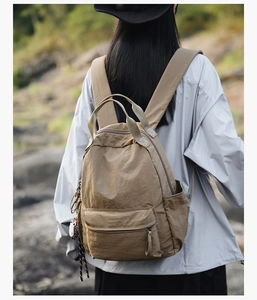 Outdoor detail of khaki nylon backpack with large main compartment and owl charm