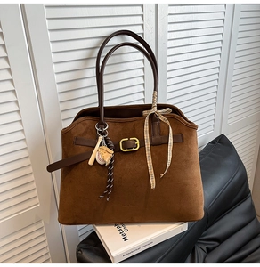 Close-up of brown suede tote bag featuring a gold square buckle and baseball charms