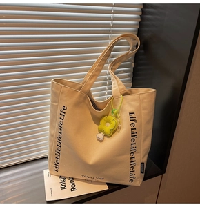 Detail of cream canvas tote bag with black letter print and a cute flower charm