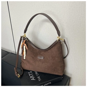 Detail einer braunen Wildleder-Hobo-Tasche mit Perlenanhänger auf einem Buch