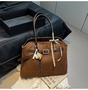 Detail view of brown suede tote bag with leather strap, metal buckle and baseball charm