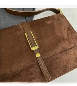 Detail of brown suede crossbody bag with gold buckle and lychee grain leather strap