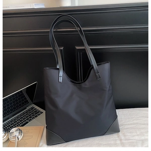 Detailed view of black nylon tote bag reinforced bottom and leather straps in office setting