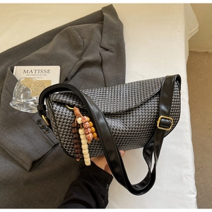 Detail of woven crossbody bag with black leather strap and decorative wood bead tassel