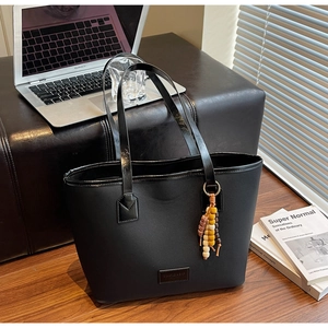 Détail du sac cabas noir avec breloque en perles de bois et logo sur un bureau en bois