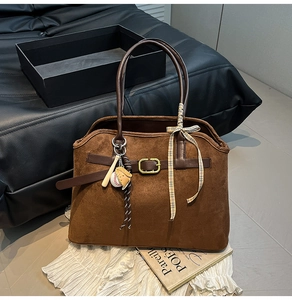 Detail of dark brown suede tote bag with leather handles and decorative baseball charms