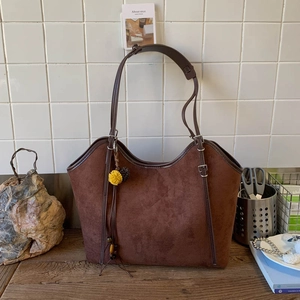 Detail of dark brown suede tote bag with yellow plush ball charm on a wooden table