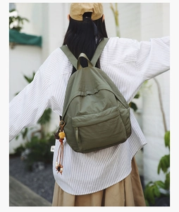 Detailed outdoor view of a dark green casual backpack with a colorful tassel charm