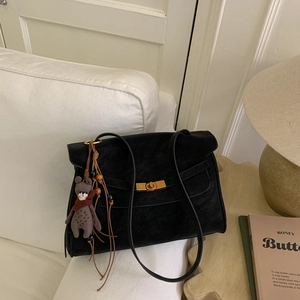 Detail of black suede shoulder bag featuring a gold twist lock and a cute bear charm