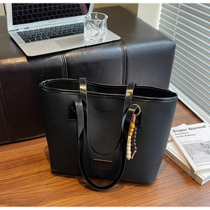Détail d'un sac cabas noir avec des perles en bois décoratives et une étiquette en cuir
