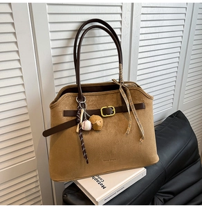 Close-up of brown suede tote bag with leather straps and decorative baseball keychain