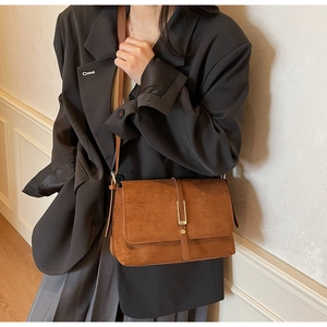 Brown suede crossbody bag with gold metal buckle detail on elegant blazer outfit
