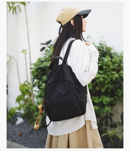 Detail view of a large black nylon backpack worn by a model in a natural outdoor setting