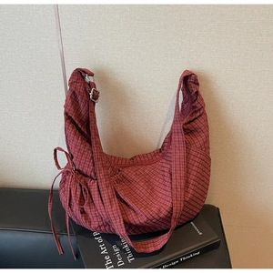 Detail view of burgundy plaid crescent bag with bow drawstring and metal strap adjustment