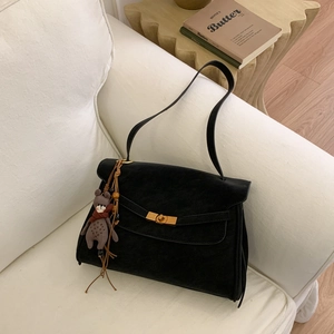 Detail of black suede handbag featuring a gold twist lock and a cute bear bag charm