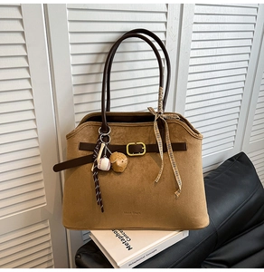 Detail of suede tote bag with brown leather strap, gold buckle and baseball charm