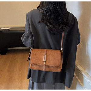 Detail of a brown suede crossbody bag with gold buckle on a model wearing a grey blazer
