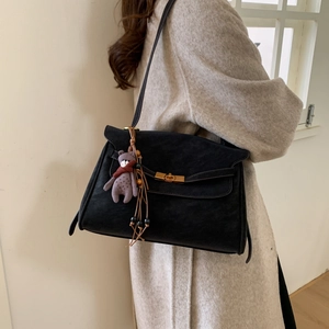 Detail of black suede shoulder bag with gold twist-lock and purple bear charm