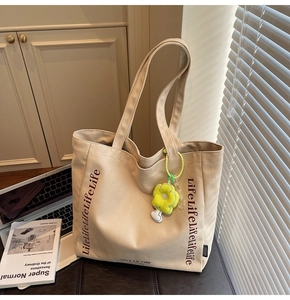 Detail of canvas tote bag featuring brown lettering and yellow flower plush charm