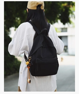 Outdoor back view of a minimalist black backpack with a yellow sunflower charm detail