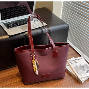 Détail du sac cabas bordeaux texturé avec pendentif perlé et logo dans un décor urbain