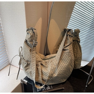 Detail of green checkered canvas crescent bag with side drawstring bow and adjustable strap
