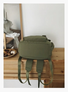 Detail view of military green nylon backpack with padded straps on a rustic wooden desk