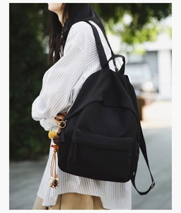 Minimalist black backpack featuring a colorful tassel charm on a striped shirt model