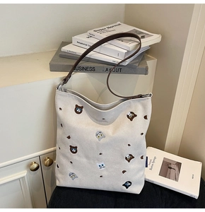 Detail of embroidered cat patterns on beige canvas tote bag with slim brown leather strap