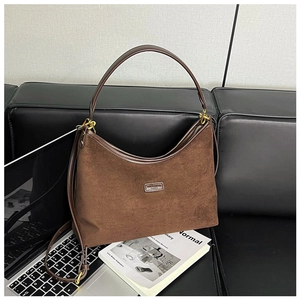 Detailansicht einer dunkelbraunen Wildleder-Hobo-Tasche mit Lederriemen auf Sofa
